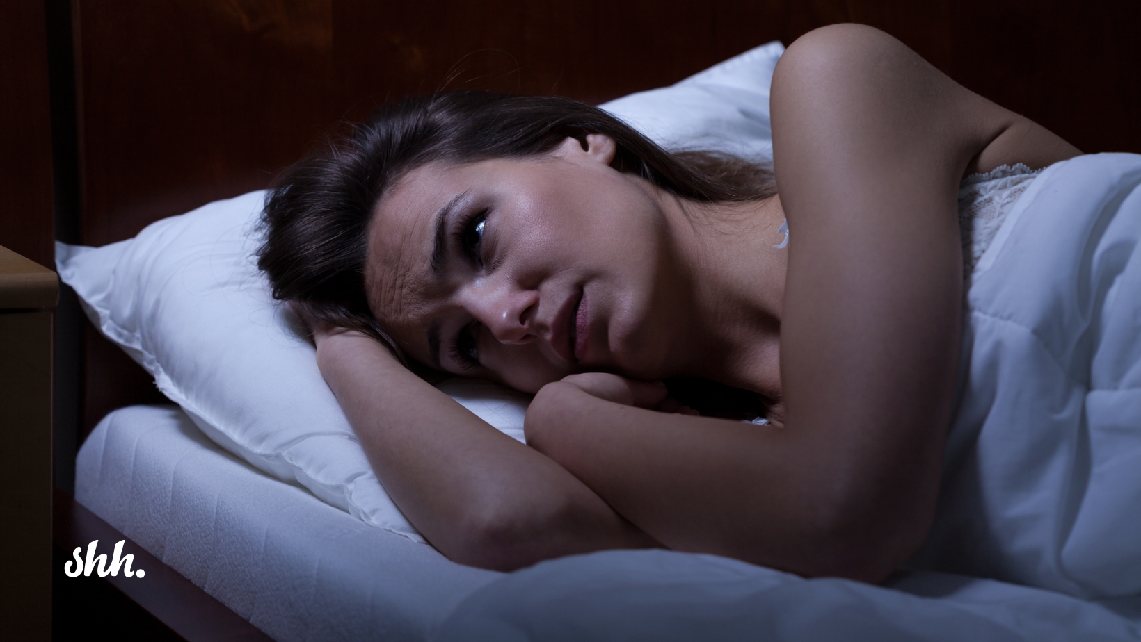 An anxious mom lies awake in bed at night, her eyes open and mind racing with overthinking as she struggles to sleep. The emotional weight of her worries is palpable, yet there's a gentle sense of hope suggesting that a guided meditation could help calm her restless mind.